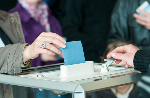 Main posant une enveloppe dans une urne pour les élections